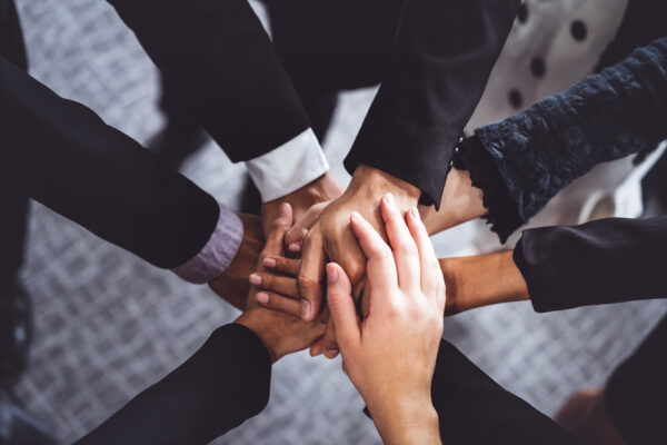 Many happy business people stacking hands together with joy and success. Company employee celebrate after finishing successful work project. Corporate partnership and achievement concept.